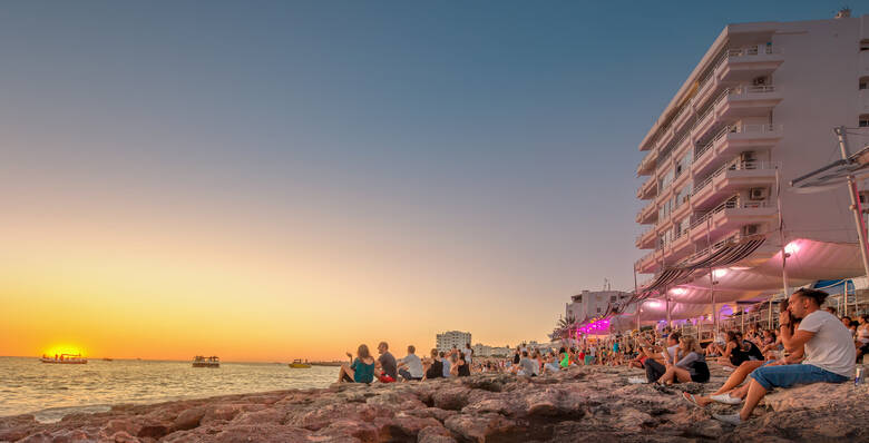 Junge Menschen schauen sich den Sonnenuntergang am Strand von Ibiza an